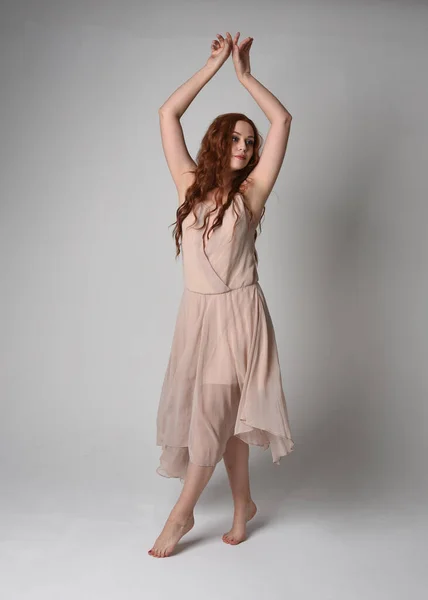 stock image Full length portrait of beautiful  female model with long  brunette hair wearing a creamy pink gown dress. graceful dancing pose, with gestural hands  isolated on white studio background.