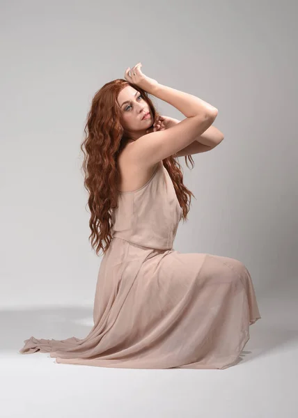 Stock image Full length portrait of beautiful brunette model  wearing a  pink dress. graceful sitting  pose, kneeling on floor gestural hands. shot from low angle perspective,  isolated on white studio background.