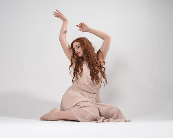 Full length portrait of beautiful brunette model  wearing a  pink dress. graceful sitting  pose, kneeling on floor gestural hands. shot from low angle perspective,  isolated on white studio background.