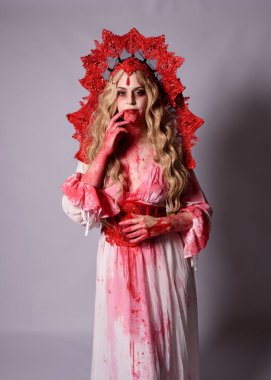 Korkunç vampir zombi kraliçenin portresi. Cadılar bayramı fantezi kostümü giymiş, kanlı kırmızı boya sıçramış. Stüdyonun arka planında el hareketleriyle kameraya uzanan izole bir şekilde..