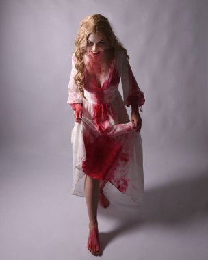  Korkunç zombi gelinin uzun bir portresi. Cadılar bayramı fantezi elbisesi ve kanlı kırmızı boya sıçraması. Ayakta durmada. Stüdyo arka planında izole edilmiş 