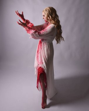  Korkunç zombi gelinin uzun bir portresi. Cadılar bayramı fantezi elbisesi ve kanlı kırmızı boya sıçraması. Ayakta durmada. Stüdyo arka planında izole edilmiş 