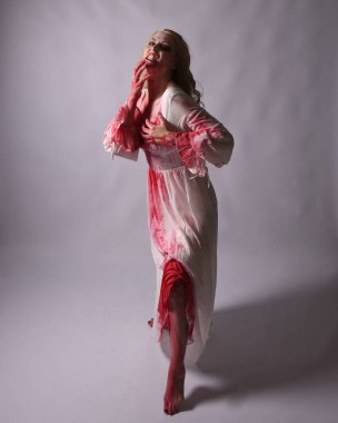  Korkunç zombi gelinin uzun bir portresi. Cadılar bayramı fantezi elbisesi ve kanlı kırmızı boya sıçraması. Ayakta durmada. Stüdyo arka planında izole edilmiş 