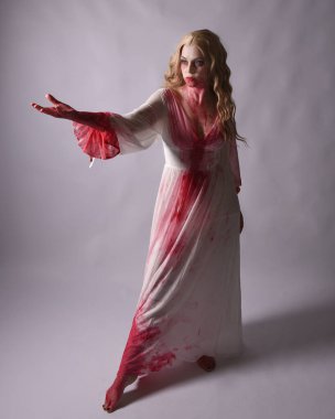  Korkunç zombi gelinin uzun bir portresi. Cadılar bayramı fantezi elbisesi ve kanlı kırmızı boya sıçraması. Ayakta durmada. Stüdyo arka planında izole edilmiş 