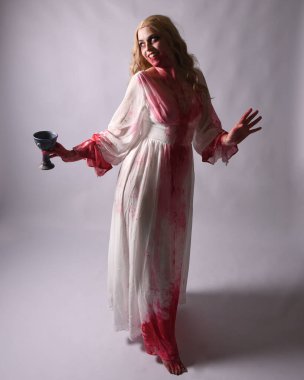  Korkunç vampir zombi gelinin portresi. Üzerinde kanlı kırmızı boya lekeleri olan şık bir Cadılar Bayramı fantazisi kostümü var. Elinde şarap kadehi var. Stüdyo arka planında izole edilmiş 