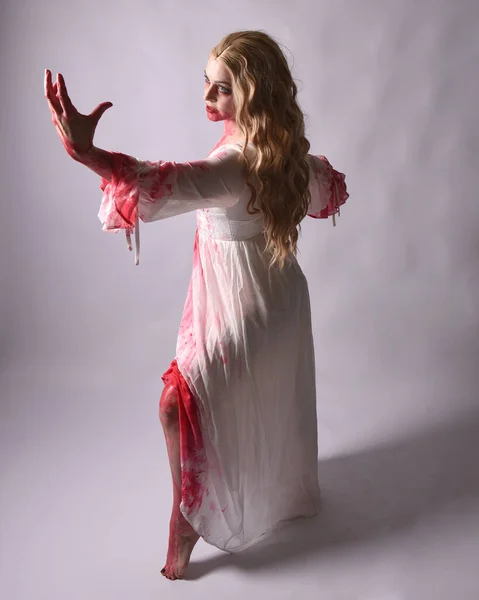 Stock image  Full length portrait of  scary vampire zombie bride, wearing elegant halloween fantasy costume  dress with bloody red paint splatter. in standing walking pose. Isolated on studio background 