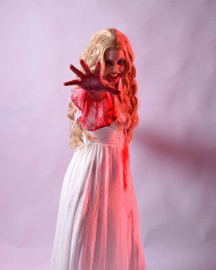 Korkunç vampir gelinin, şık cadılar bayramı fantezi kostümlü, kanlı sıçrayan portresi. Stüdyonun arka planında el hareketleriyle kameraya uzanan izole bir şekilde..