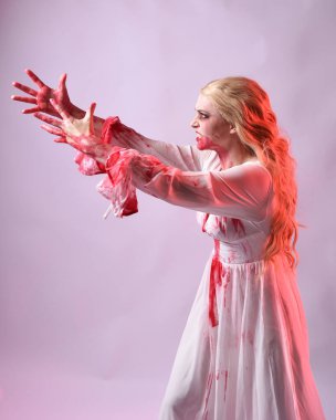 Korkunç vampir gelinin, şık cadılar bayramı fantezi kostümlü, kanlı sıçrayan portresi. Stüdyonun arka planında el hareketleriyle kameraya uzanan izole bir şekilde..