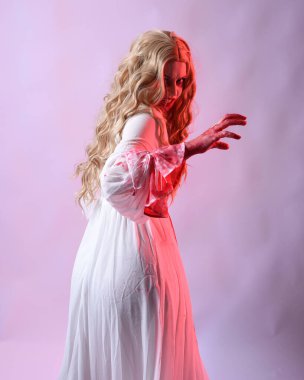 Korkunç vampir gelinin, şık cadılar bayramı fantezi kostümlü, kanlı sıçrayan portresi. Stüdyonun arka planında el hareketleriyle kameraya uzanan izole bir şekilde..