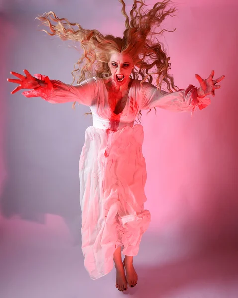 stock image Full length portrait scary vampire zombie bride wearing bloody halloween fantasy costume dress. Dynamic jumping pose gestural arms reaching out. Isolated  studio backdrop with cinematic red lighting.