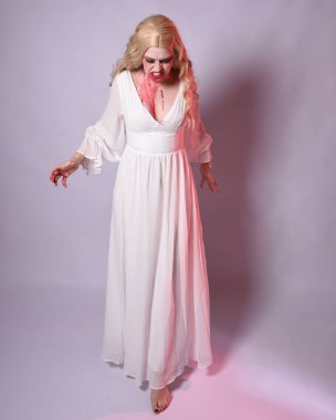  Korkunç zombi gelinin uzun bir portresi. Cadılar bayramı fantezi elbisesi ve kanlı kırmızı boya sıçraması. Ayakta durma pozu. Beyaz stüdyo arka planında izole edilmiş. 