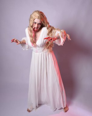  Korkunç zombi gelinin uzun bir portresi. Cadılar bayramı fantezi elbisesi ve kanlı kırmızı boya sıçraması. Ayakta durma pozu. Beyaz stüdyo arka planında izole edilmiş. 