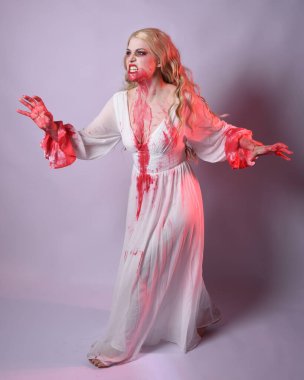  Korkunç zombi gelinin uzun bir portresi. Cadılar bayramı fantezi elbisesi ve kanlı kırmızı boya sıçraması. Ayakta durma pozu. Beyaz stüdyo arka planında izole edilmiş. 