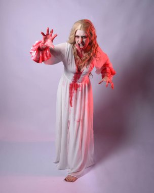  Korkunç zombi gelinin uzun bir portresi. Cadılar bayramı fantezi elbisesi ve kanlı kırmızı boya sıçraması. Ayakta durma pozu. Beyaz stüdyo arka planında izole edilmiş. 