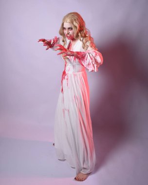  Korkunç zombi gelinin uzun bir portresi. Cadılar bayramı fantezi elbisesi ve kanlı kırmızı boya sıçraması. Ayakta durma pozu. Beyaz stüdyo arka planında izole edilmiş. 