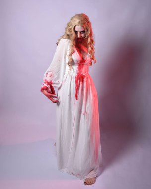  Korkunç zombi gelinin uzun bir portresi. Cadılar bayramı fantezi elbisesi ve kanlı kırmızı boya sıçraması. Ayakta durma pozu. Beyaz stüdyo arka planında izole edilmiş. 