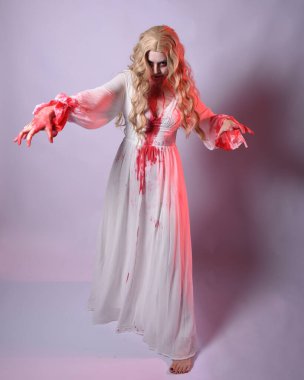  Korkunç zombi gelinin uzun bir portresi. Cadılar bayramı fantezi elbisesi ve kanlı kırmızı boya sıçraması. Ayakta durma pozu. Beyaz stüdyo arka planında izole edilmiş. 
