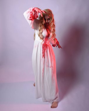  Korkunç zombi gelinin uzun bir portresi. Cadılar bayramı fantezi elbisesi ve kanlı kırmızı boya sıçraması. Ayakta durma pozu. Beyaz stüdyo arka planında izole edilmiş. 