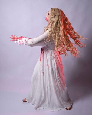  Korkunç zombi gelinin uzun bir portresi. Cadılar bayramı fantezi elbisesi ve kanlı kırmızı boya sıçraması. Ayakta durma pozu. Beyaz stüdyo arka planında izole edilmiş. 