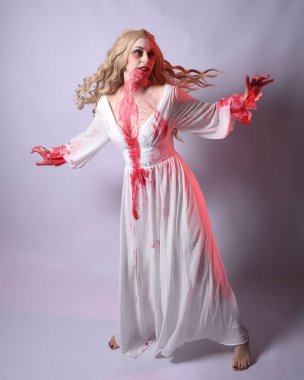  Korkunç zombi gelinin uzun bir portresi. Cadılar bayramı fantezi elbisesi ve kanlı kırmızı boya sıçraması. Ayakta durma pozu. Beyaz stüdyo arka planında izole edilmiş. 