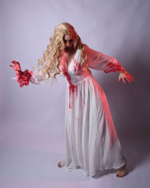  Korkunç zombi gelinin uzun bir portresi. Cadılar bayramı fantezi elbisesi ve kanlı kırmızı boya sıçraması. Ayakta durma pozu. Beyaz stüdyo arka planında izole edilmiş. 