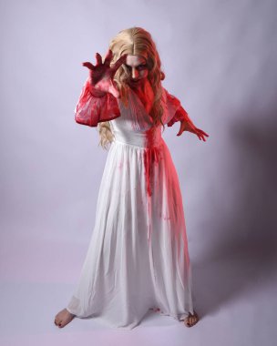  Korkunç zombi gelinin uzun bir portresi. Cadılar bayramı fantezi elbisesi ve kanlı kırmızı boya sıçraması. Ayakta durma pozu. Beyaz stüdyo arka planında izole edilmiş. 