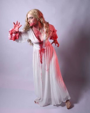  Korkunç zombi gelinin uzun bir portresi. Cadılar bayramı fantezi elbisesi ve kanlı kırmızı boya sıçraması. Ayakta durma pozu. Beyaz stüdyo arka planında izole edilmiş. 