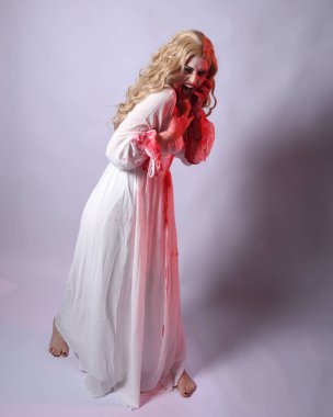  Korkunç zombi gelinin uzun bir portresi. Cadılar bayramı fantezi elbisesi ve kanlı kırmızı boya sıçraması. Ayakta durma pozu. Beyaz stüdyo arka planında izole edilmiş. 