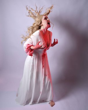  Korkunç zombi gelinin uzun bir portresi. Cadılar bayramı fantezi elbisesi ve kanlı kırmızı boya sıçraması. Ayakta durma pozu. Beyaz stüdyo arka planında izole edilmiş. 