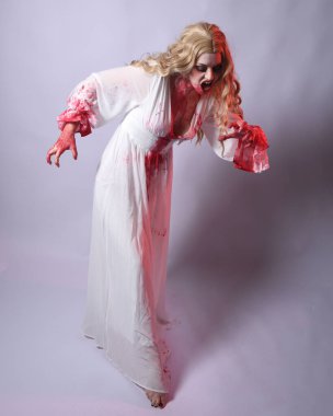  Korkunç zombi gelinin uzun bir portresi. Cadılar bayramı fantezi elbisesi ve kanlı kırmızı boya sıçraması. Ayakta durma pozu. Beyaz stüdyo arka planında izole edilmiş. 