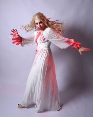  Korkunç zombi gelinin uzun bir portresi. Cadılar bayramı fantezi elbisesi ve kanlı kırmızı boya sıçraması. Ayakta durma pozu. Beyaz stüdyo arka planında izole edilmiş. 