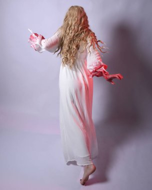  Korkunç zombi gelinin uzun bir portresi. Cadılar bayramı fantezi elbisesi ve kanlı kırmızı boya sıçraması. Ayakta durma pozu. Beyaz stüdyo arka planında izole edilmiş. 