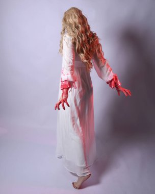  Korkunç zombi gelinin uzun bir portresi. Cadılar bayramı fantezi elbisesi ve kanlı kırmızı boya sıçraması. Ayakta durma pozu. Beyaz stüdyo arka planında izole edilmiş. 