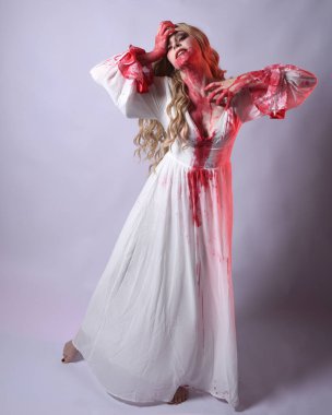  Korkunç zombi gelinin uzun bir portresi. Cadılar bayramı fantezi elbisesi ve kanlı kırmızı boya sıçraması. Ayakta durma pozu. Beyaz stüdyo arka planında izole edilmiş. 