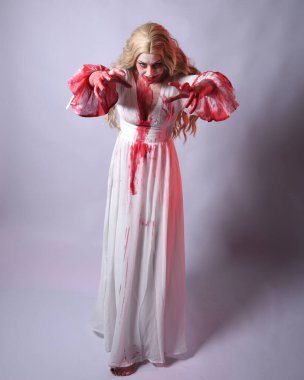  Korkunç zombi gelinin uzun bir portresi. Cadılar bayramı fantezi elbisesi ve kanlı kırmızı boya sıçraması. Ayakta durma pozu. Beyaz stüdyo arka planında izole edilmiş. 