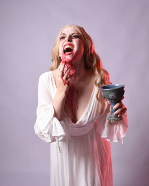  Korkunç zombi gelinin uzun bir portresi. Cadılar bayramı fantezi elbisesi ve kanlı kırmızı boya sıçraması. Ayakta durma pozu. Beyaz stüdyo arka planında izole edilmiş. 