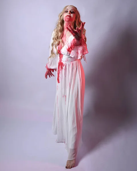 stock image  Full length portrait of  scary vampire zombie bride, wearing elegant halloween fantasy costume  dress with bloody red paint splatter. standing walking pose. Isolated on white studio background 