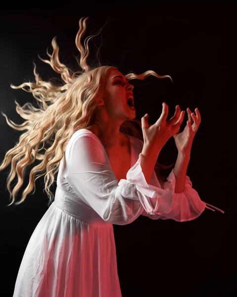 Zarif beyaz cadılar bayramı fantezi elbisesi giymiş korkunç sarışın vampir gelinin portresi. Karanlık stüdyo arka planında, endişeli hareketli eller uzanıyor. 