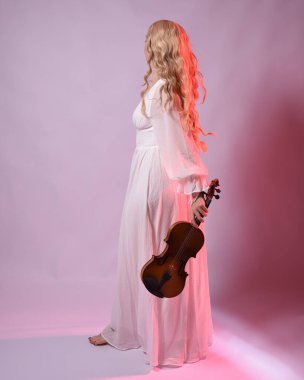 Zarif beyaz cadılar bayramı elbisesi giyen güzel sarışın mankenin tam boy portresi, tarihi fantezi karakteri. ... arka planda izole edilmiş bir keman enstrümanı tutarken....