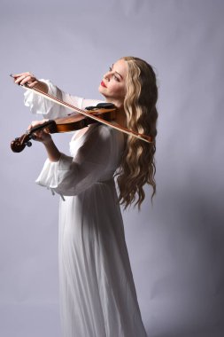Zarif beyaz cadılar bayramı elbisesi giyen güzel sarışın mankenin yakın plan portresi. Tarihi bir fantezi karakteri. Stüdyonun arka planında izole edilmiş bir keman enstrümanı tutuyor..