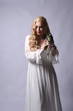 Zarif beyaz cadılar bayramı elbisesi giyen güzel sarışın mankenin yakın plan portresi. Tarihi bir fantezi karakteri. Şarap kadehi, ses arkaplanda izole..