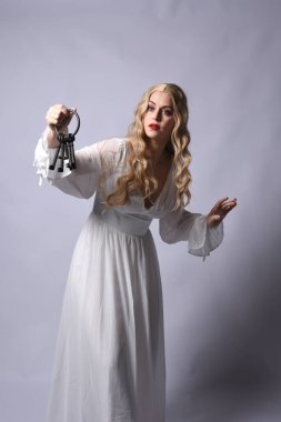 Close up portrait of beautiful blonde model wearing elegant  white halloween gown, a historical fantasy character. Holding old key chain, isolated on studio background. clipart