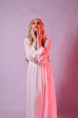 Zarif beyaz cadılar bayramı elbisesi giyen güzel sarışın mankenin yakın portresi. Aç vampir gibi uzanan kollar. Kırmızı karamsar ışıklandırma ile stüdyo arka planında izole.