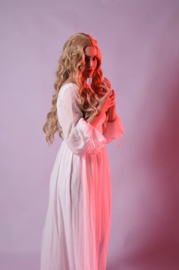 Zarif beyaz cadılar bayramı elbisesi giyen güzel sarışın mankenin yakın portresi. Aç vampir gibi uzanan kollar. Kırmızı karamsar ışıklandırma ile stüdyo arka planında izole.