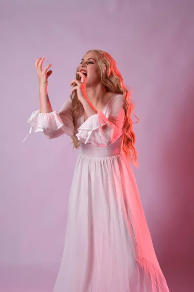 stock image Close up portrait of beautiful blonde model wearing elegant  white halloween gown. arms reaching out like hungry vampire.  isolated on studio background with  red cinematic moody lighting.