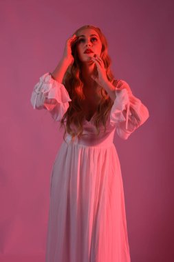 Zarif beyaz cadılar bayramı elbisesi giyen güzel sarışın mankenin yakın portresi. Aç vampir gibi uzanan kollar. Kırmızı karamsar ışıklandırma ile stüdyo arka planında izole.