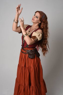 Ortaçağ bakiresi giymiş güzel kızıl saçlı bir kadının portresi. Falcı kostümü. El hareketleriyle poz vermek, dans etmek, stüdyo arka planında soyutlanmak..