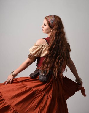 Ortaçağ bakiresi giymiş güzel kızıl saçlı bir kadının portresi. Falcı kostümü. El hareketleriyle poz vermek, dans etmek, stüdyo arka planında soyutlanmak..