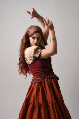 Ortaçağ bakiresi giymiş güzel kızıl saçlı bir kadının portresi. Falcı kostümü. El hareketleriyle poz vermek, dans etmek, stüdyo arka planında soyutlanmak..