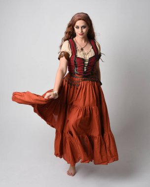 Ortaçağ bakiresi, falcı kostümü giymiş güzel kızıl saçlı bir kadının tam boy portresi. Dans hareketleriyle ayakta durmak, etek sallamak. Stüdyo arka planında izole.